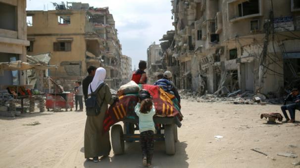 Des Palestiniens transportent leurs affaires sur un chariot entre des bâtiments détruits à Khan Younès, dans le sud de la bande de Gaza, le 2 mai 2024