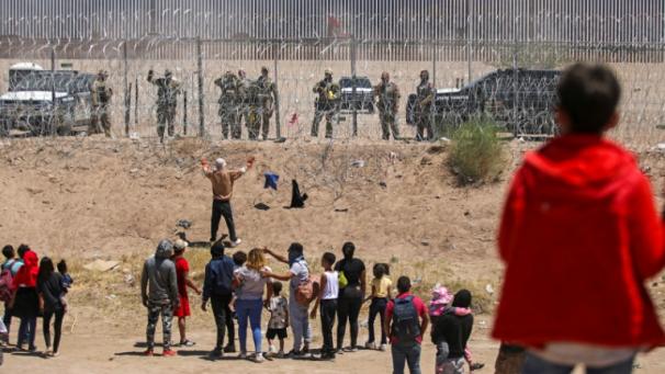 Des migrants cherchant à entrer aux Etats-Unis devant une barrière de fil barbelé et des agents de la Garde nationale du Texas, à la frontière entre le Mexique et les Etats-Unis, à Ciudad Juarez, le 13 mai 2024